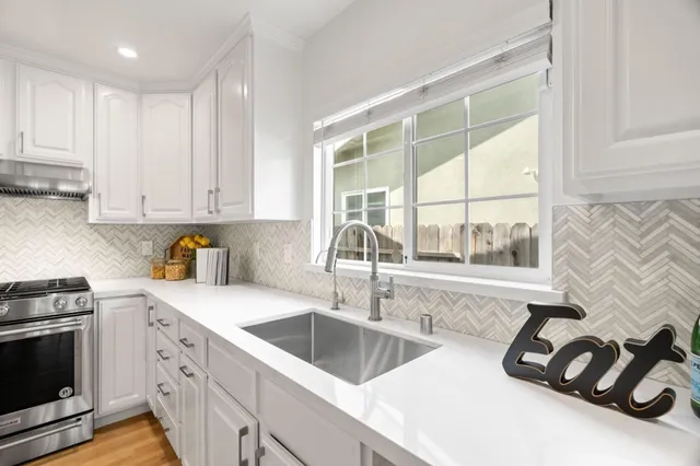 a kitchen with stainless steel appliances a sink a stove and a white counter tops with wooden floors