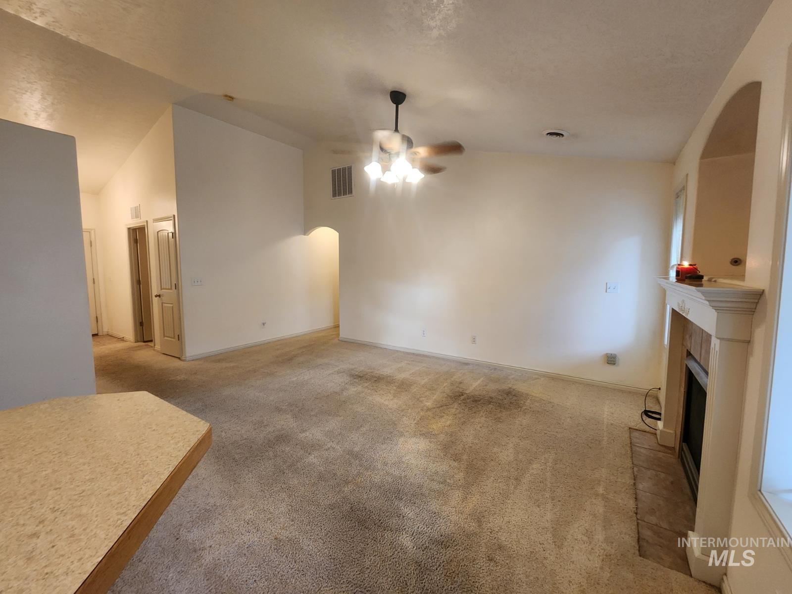 1000 North Rodeo Street Parma, ID 83660 - Photo 10 of 35 Unfurnished living room with ceiling fan, lofted ceiling, arched walkways, carpet, and a fireplace with raised hearth