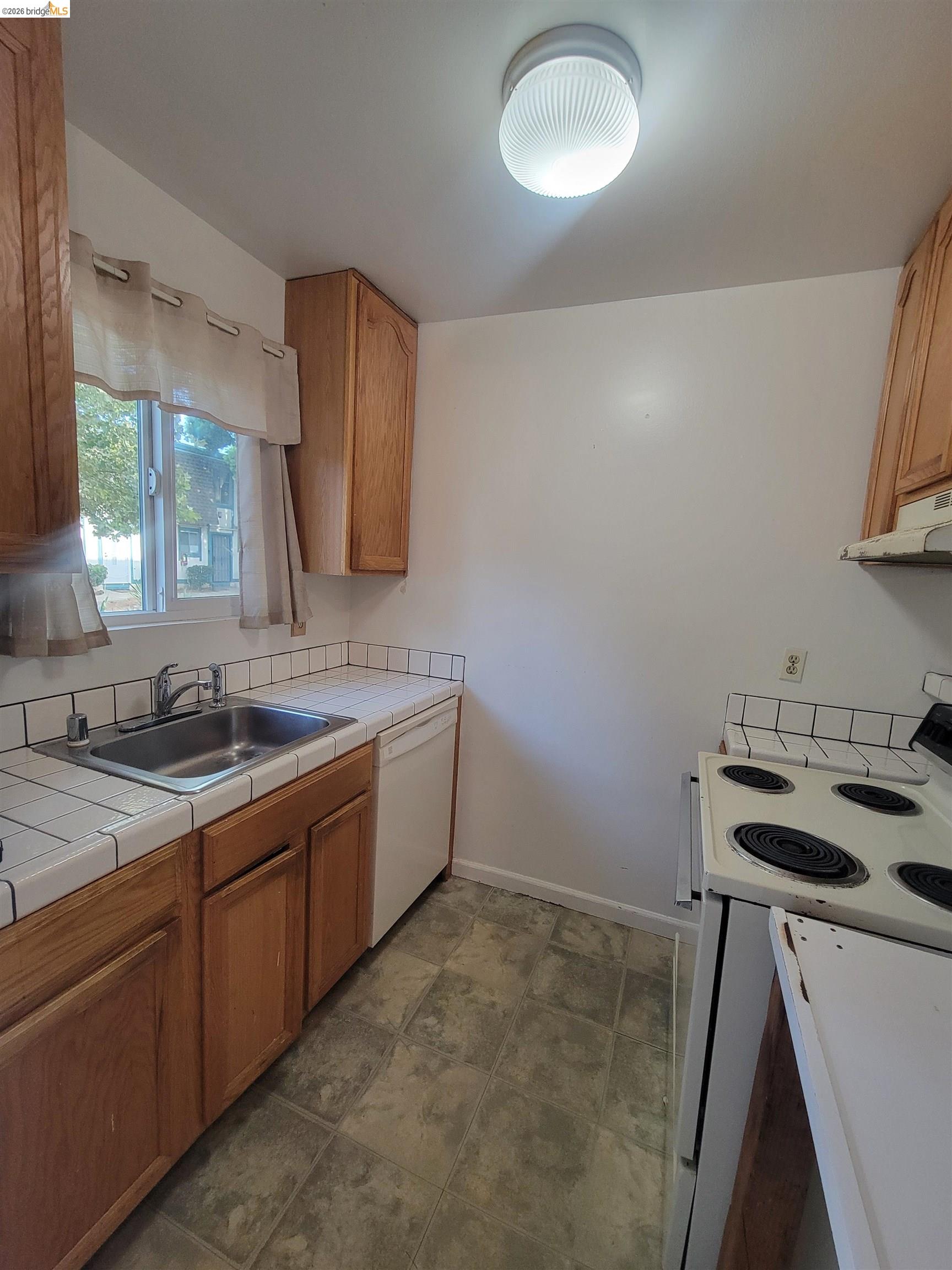3905 Clayton Road, Unit 12 Concord, CA 94521 - Photo 9 of 21 Kitchen featuring wood cabinetry, a stainless steel sink, white tiled countertops with a matching backsplash, and a white dishwasher