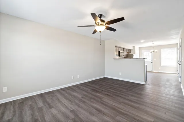 a view of an empty room with wooden floor and a ceiling fan