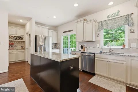 a kitchen with stainless steel appliances granite countertop a refrigerator a sink dishwasher a stove and white cabinets with wooden floor