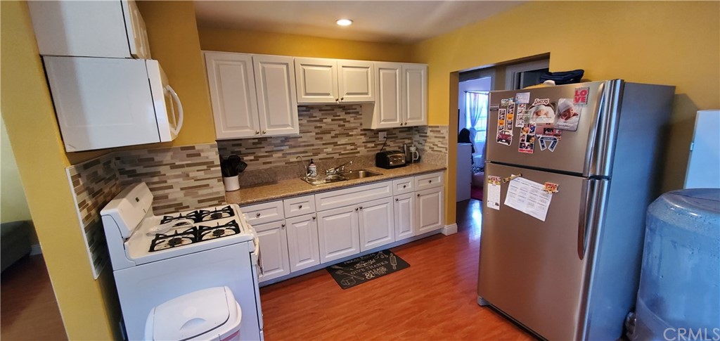 a kitchen with stainless steel appliances a refrigerator a sink a stove a refrigerator white cabinets and wooden floor