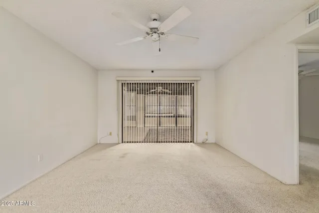an empty room with chandelier fan and windows