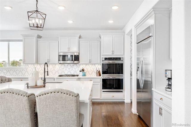 a kitchen with stainless steel appliances kitchen island granite countertop a refrigerator a stove a sink and white cabinets with wooden floor