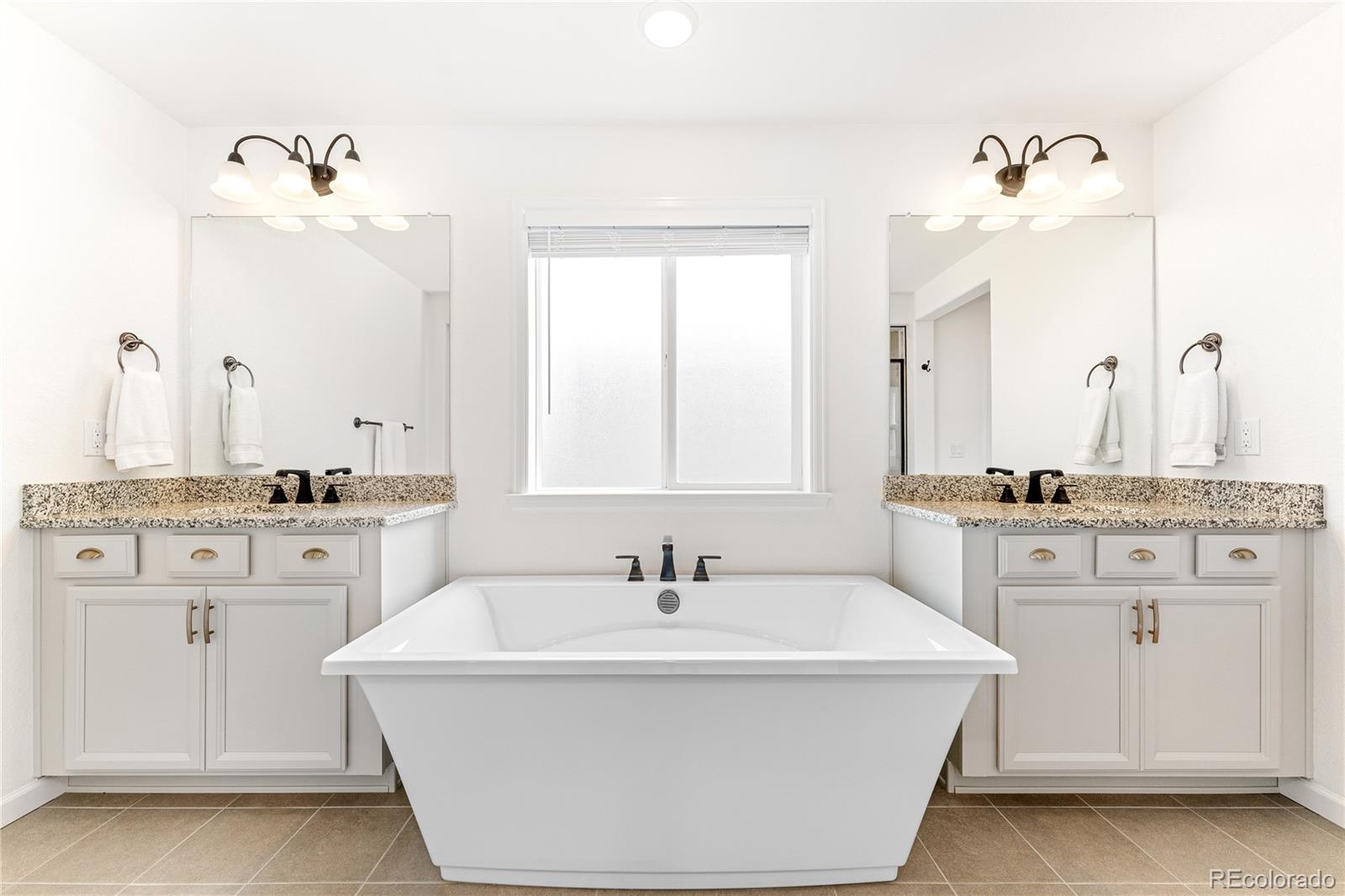 16391 Buffalo Run Drive Commerce City, CO 80022 - Photo 24 of 49 a bathroom with a double vanity sink a mirror and a bathtub