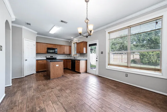 a open kitchen with stainless steel appliances granite countertop a stove top oven a sink dishwasher a refrigerator and a dining table with wooden floor