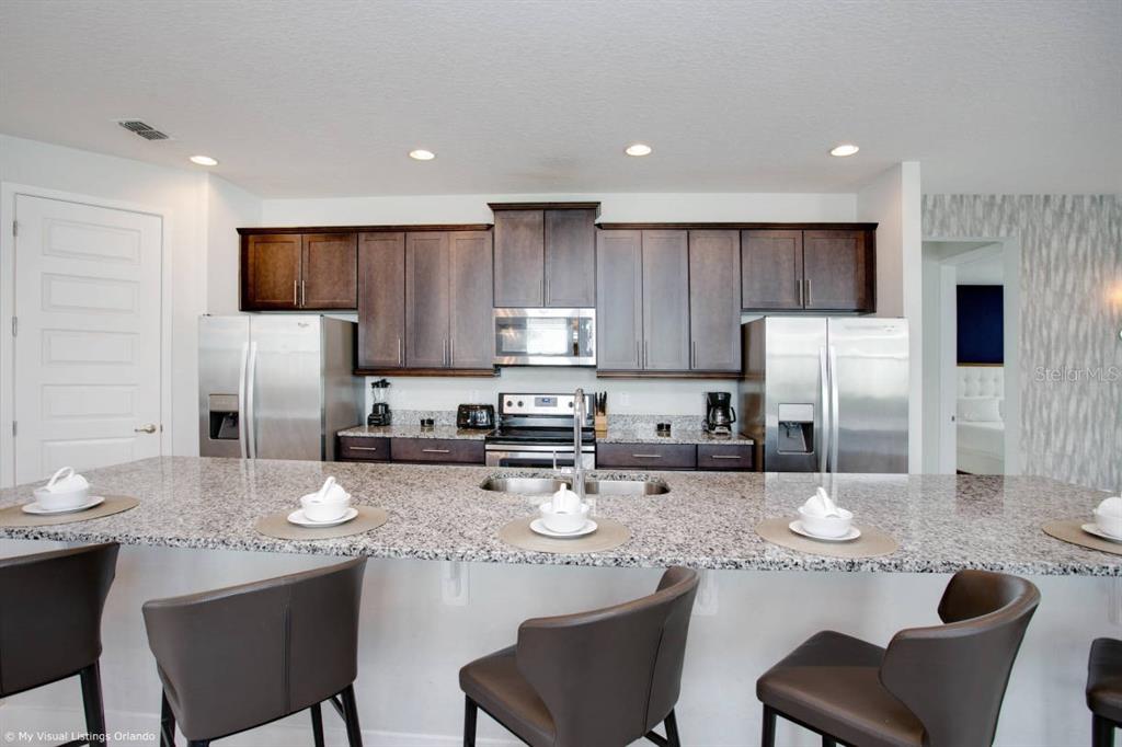 7736 Graben Street Kissimmee, FL 34747 - Photo 44 of 62 a kitchen with stainless steel appliances granite countertop a dining table chairs sink refrigerator and microwave