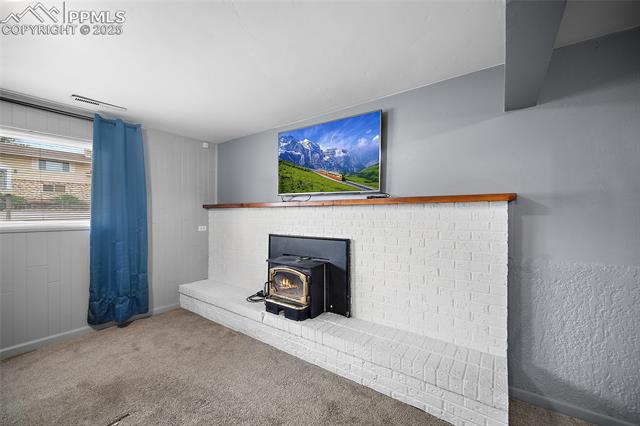 1921 Wooten Road Colorado Springs, CO 80915 - Photo 8 of 49 Unfurnished living room featuring a wood stove, carpet flooring, and wooden walls