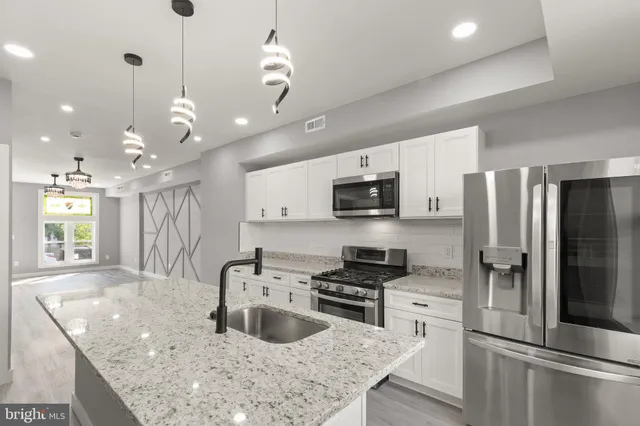 a kitchen with stainless steel appliances granite countertop a sink a stove a refrigerator and island with wooden floor