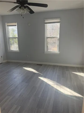 an empty room with wooden floor fan and windows