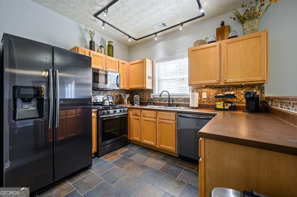a kitchen with stainless steel appliances granite countertop a refrigerator a sink dishwasher a stove and a dining table with wooden floor