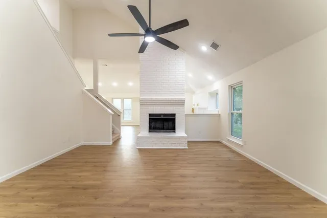 an empty room with wooden floor a ceiling fan a fireplace and windows