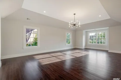 an empty room with wooden floor chandelier and windows
