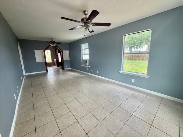 an empty room with chandelier fan and windows