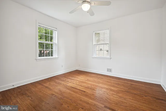 an empty room with wooden floor chandelier fan and windows