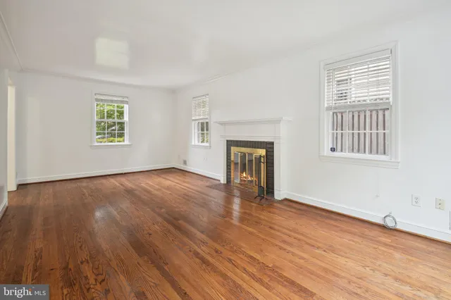 an empty room with wooden floor fireplace and windows