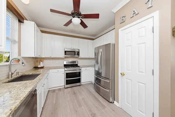 a kitchen with stainless steel appliances granite countertop a refrigerator oven a sink dishwasher and white cabinets with wooden floor