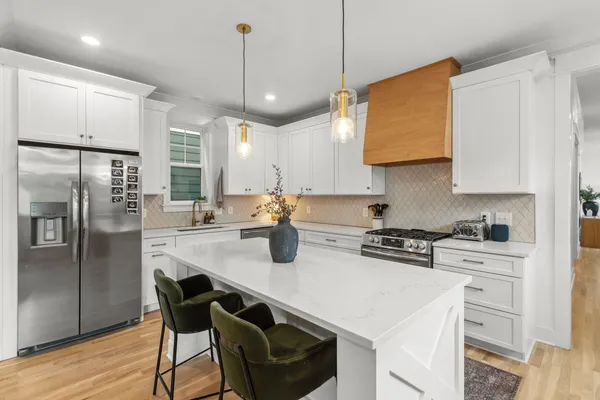a kitchen with stainless steel appliances granite countertop a stove a refrigerator a sink a stove and white cabinets with wooden floor