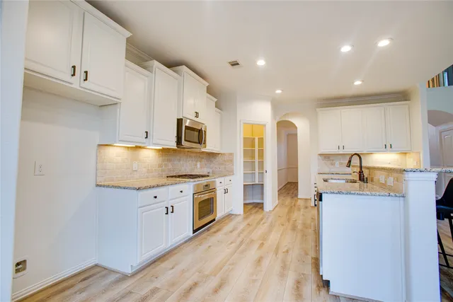 a large kitchen with stainless steel appliances granite countertop a lot of counter space and wooden floors