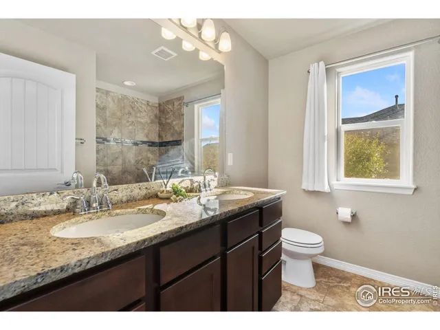 a bathroom with a granite countertop sink a toilet a mirror and a window