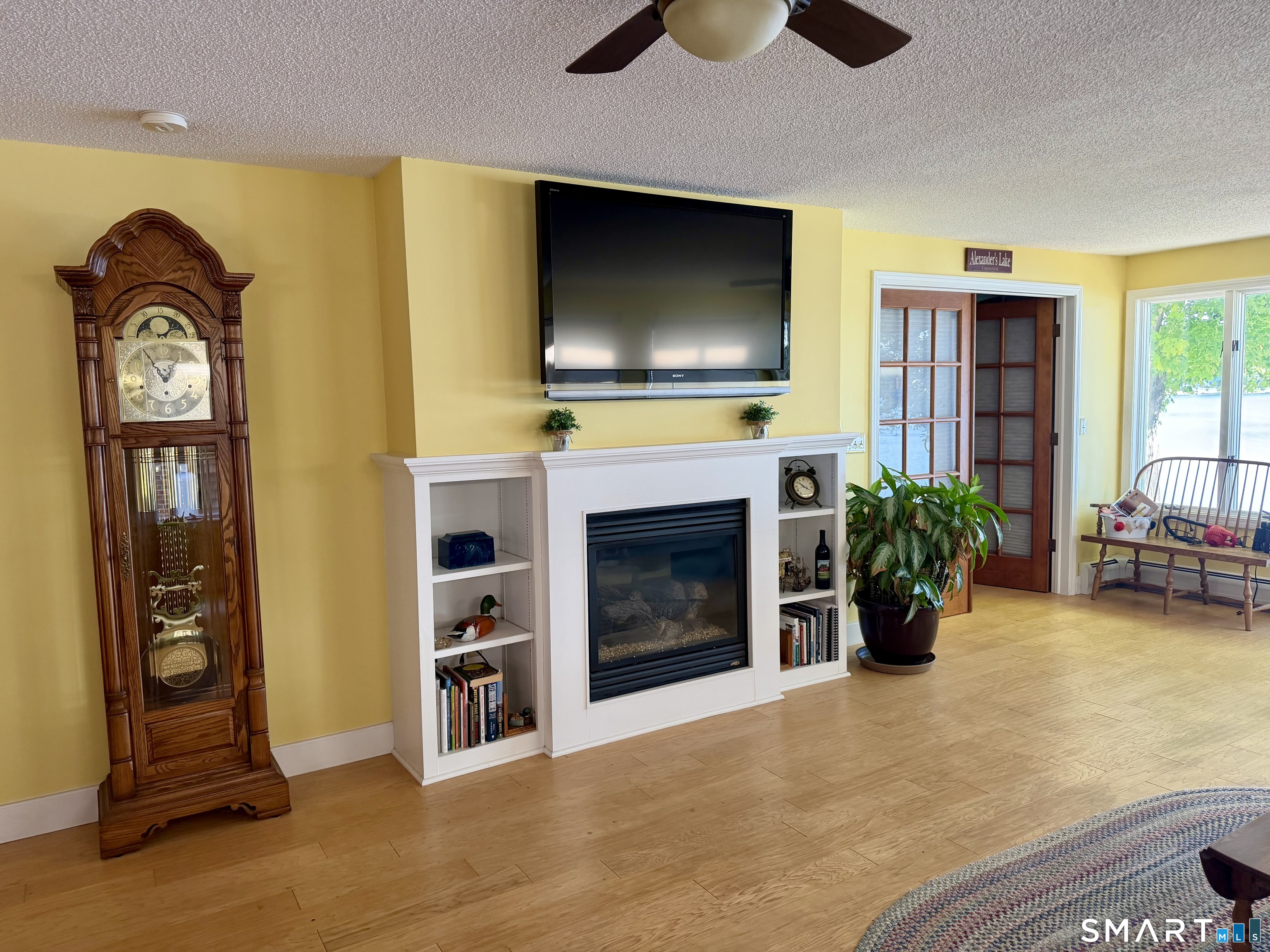204 Pine Hollow Road Killingly, CT 06241 - Photo 12 of 20 The inviting living room features warm wood flooring, a fireplace with built-in shelving, a ceiling fan and French doors. With natural light and Alexander's Lake just outside, this is a comfortable place to gather in every season