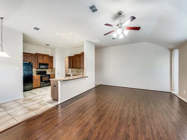 a view of an empty room with kitchen appliances and a ceiling fan