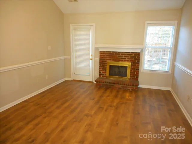 an empty room with wooden floor fireplace and windows