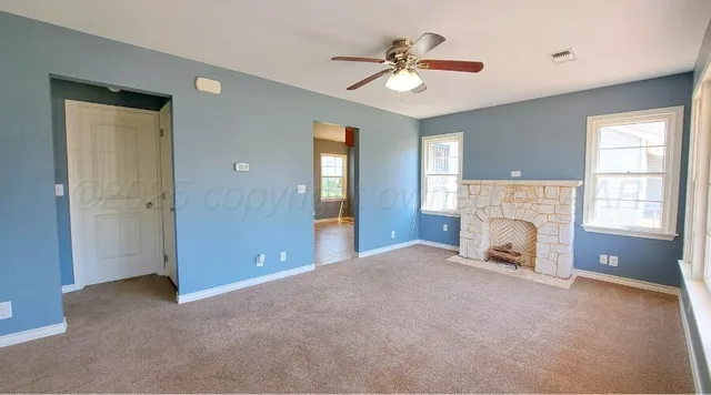 a view of a livingroom with a fireplace ceiling fan and windows