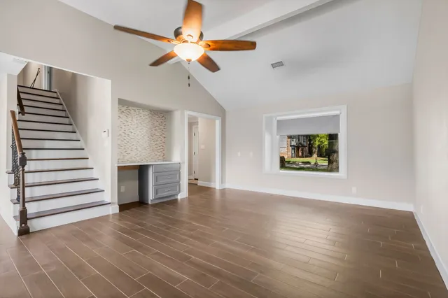 an empty room with wooden floor chandelier fan and windows