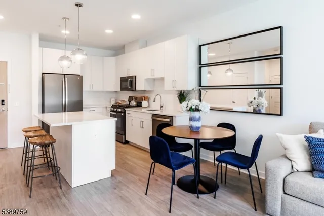 a kitchen with stainless steel appliances kitchen island granite countertop a dining table chairs and a refrigerator