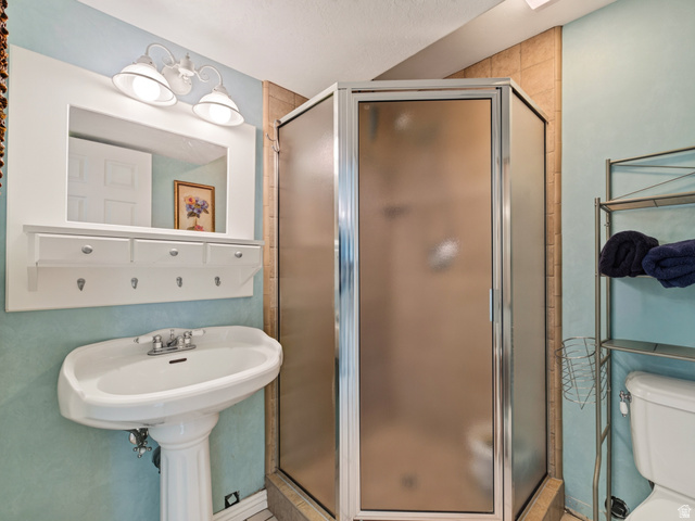 4380 Main Street Logan, UT 84321 - Photo 48 of 74 Basement bathroom with pedestal sink, chrome faucet, wall-mounted mirror with integrated lighting, built-in shelving with hooks, and a corner shower with frosted glass enclosure
