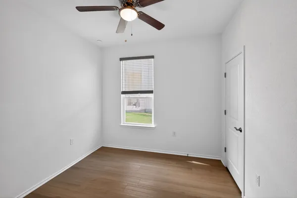 an empty room with wooden floor fan and windows