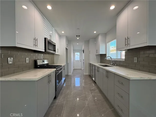 a large kitchen with stainless steel appliances granite countertop a sink a stove a refrigerator and white cabinets