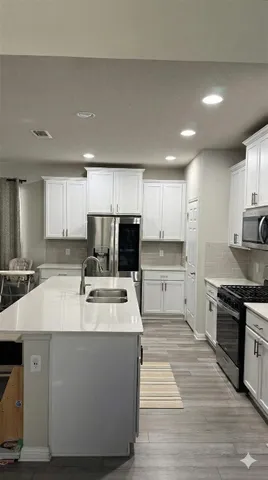 a large kitchen with stainless steel appliances granite countertop a stove a sink a refrigerator and white cabinets with wooden floor