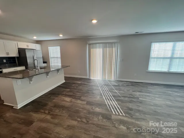 a view of kitchen and empty room with wooden floor and window