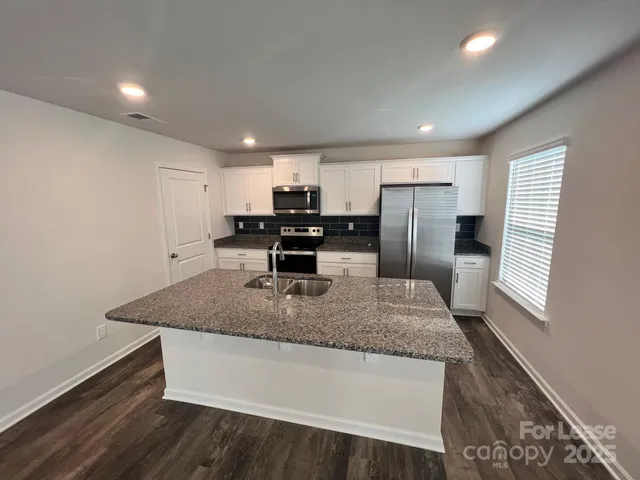 a kitchen with stainless steel appliances granite countertop a sink dishwasher a refrigerator and a stove with wooden floor
