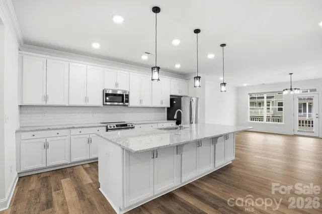 a large kitchen with stainless steel appliances kitchen island granite countertop a stove a sink and white cabinets with wooden floor