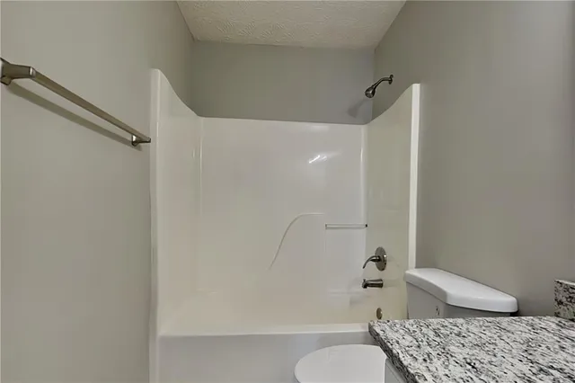 a bathroom with a granite countertop bathtub shower and toilet