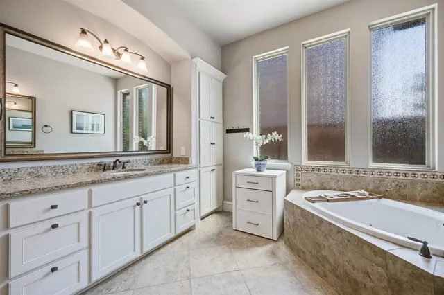 a bathroom with a granite countertop double vanity sink a mirror and a bathtub