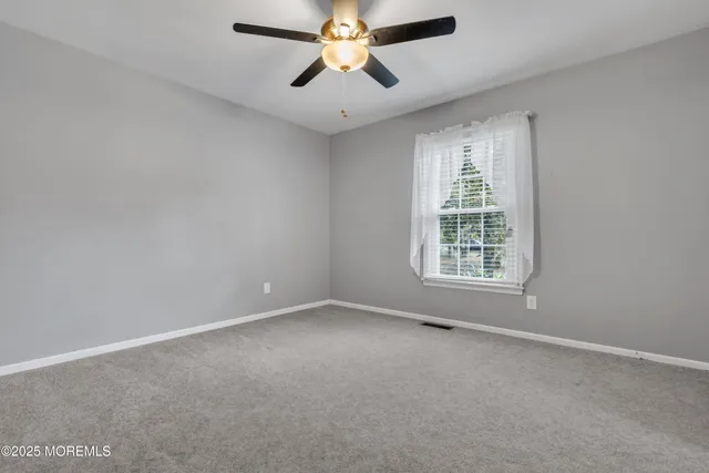 an empty room with chandelier fan and windows