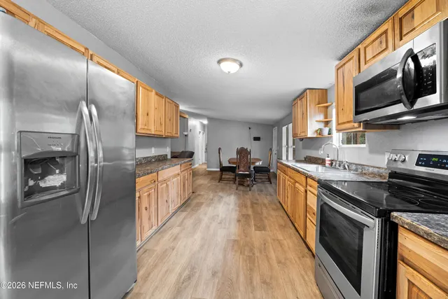 a kitchen with stainless steel appliances a stove top oven a sink a refrigerator white cabinets and wooden floor