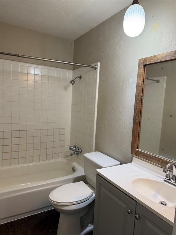 3801 Guthrie Road Garland, TX 75043 - Photo 13 of 24 Bathroom featuring a built-in tub with tile surround, a white toilet, a vanity with a white countertop and integrated sink, and a wood-framed mirror
