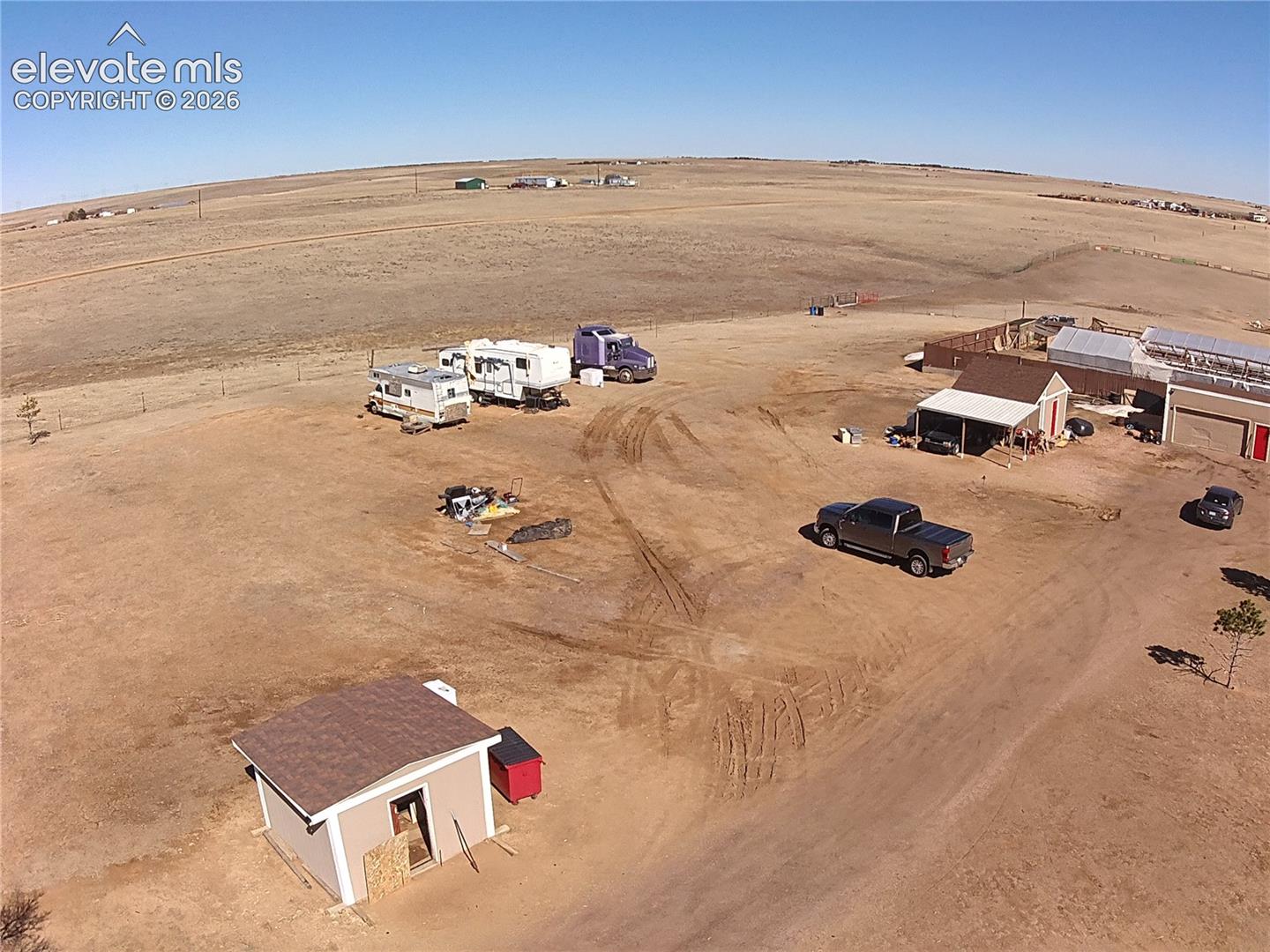 3835 Sengbeil Road Yoder, CO 80864 - Photo 41 of 48 Expansive open land featuring multiple structures, including a small building with a shingle roof, an L-shaped building with a brown shingle roof and covered porch, and a larger structure with a metal roof and red garage doors
