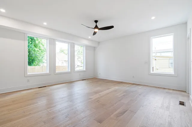 an empty room with wooden floor ceiling fan and windows