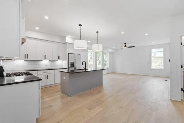 a kitchen with stainless steel appliances granite countertop a stove a sink a refrigerator and white cabinets with wooden floor