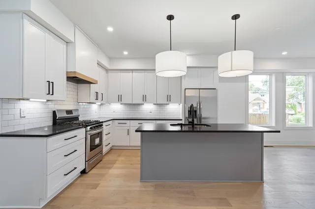 a kitchen with stainless steel appliances granite countertop a sink a stove a refrigerator and white cabinets