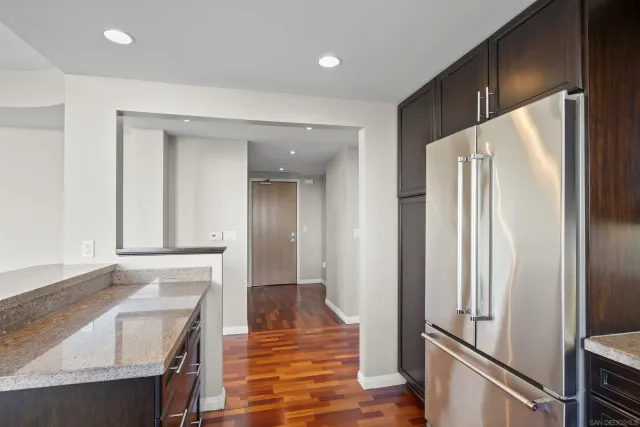 a kitchen with stainless steel appliances granite countertop a refrigerator a sink dishwasher a stove and a dining table with wooden floor