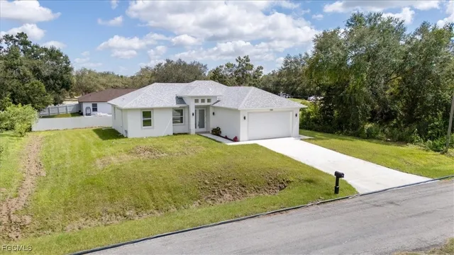 a view of a white house in front of a big yard plants and large trees