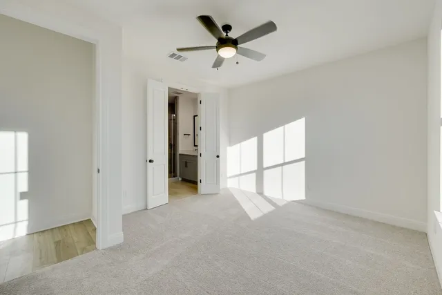 an empty room with chandelier fan and windows