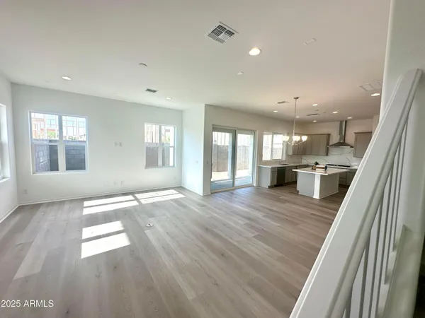 a view of an empty room and kitchen with wooden floor